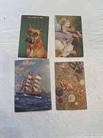 Four early 1900s postcards displaying a boxer dog portrait, children with dolls, a sailing ship, and sea-themed shells and starfish.