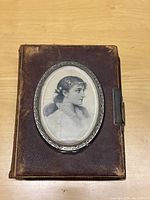 Front cover of the 19th century cabinet photo album showing leather binding, oval beveled glass with portrait underneath, and wear on the edges.