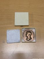 Top-down photo of the bronze medal inside original white box with cushioned insert.