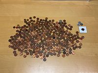 Large spread of mostly copper pennies scattered on a table, with some zinc pennies and miscellaneous coins off to the side.