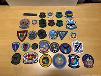 Thirty US military patches arranged in rows on a wooden surface including Desert Storm and US Air Force units, showing colors and designs.