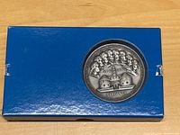 Blue box with silver medal embedded on lid showing multiple historical figures in profile and buildings below