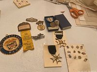 Various civilian and military medals, badges, and pins arranged on a table with scissors and papers in background