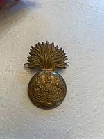 Front view of the heavy brass Royal Scottish Fusiliers hat badge showing detailed embossed crest, crowned top and supporting animals, plus flaming grenade design top.