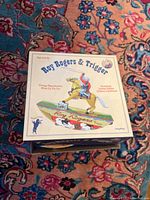 Top view of vintage reproduction Schylling Roy Rogers & Trigger tin toy box with colorful artwork and text.