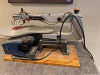 Side view of Ryobi scroll saw showing the metal frame mounted on a wooden base with electrical cord and saw blade in place.