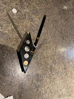 Wide view showing black rhombus-shaped stand with four coins and black gold-accented pen inserted upright.