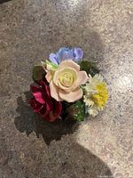 Top angled photo showing multicolored floral bone china figurine including pale pink rose, red rose, yellow carnation, blue flower, and green leaves.