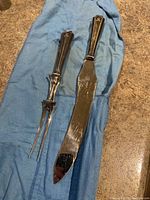 Full view of the carving fork and carving knife lying on a blue cloth on brown surface.