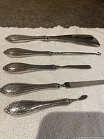 Full set of five sterling silver vanity tools with decorative handles laid on white towel.