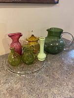 Full group of colored glass items displayed on clear glass tray, shown on countertop.