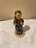 Front view of the Hummel figurine showing detailed painting and facial features with black hat, rifle and basket.