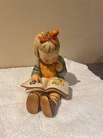 Front view of the Hummel figurine of a girl reading a book, showing her seated with all details visible including attire and open book images.