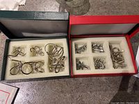 Two open boxes showing various metal impossible puzzles made of bent metal pieces in foam compartments.