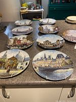 View of 10 hand-painted Limoges porcelain collector plates arranged on kitchen counter, each depicting various European famous landmarks and cityscapes.