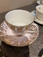 Close-up of Adderley fine bone china tea cup with white and gold floral design and scalloped edges.