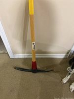 Full view of pick axe with wooden handle, metal head, and red grip section.
