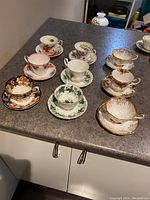 Full set of five Royal Albert teacup and saucer pairs laid on countertop showing various floral and ornate patterns in different colors.