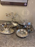 Group photo of silver plated candelabra and assorted silver plated serving pieces including covered dishes, pitcher, and bowls.