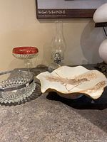 Four items on countertop: glass oil lamp, glass bowl with metal rim, decorative glass dish, ceramic dish with leaf design.