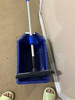 Blue plastic bucket with handle and wringer, showing the squeegee handle resting inside.