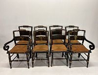 Full view of all eight black wooden stenciled dining chairs with rush seats arranged in two rows showing overall condition and group composition.