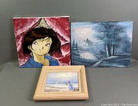 Three oil paintings displayed together; one anime portrait, one blue landscape, one framed seaside scene.