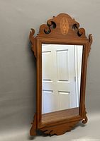 Full view of Chippendale style wall mirror showing its wooden frame with decorative carved scrolls and inlaid top crest.