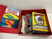Red box containing a stack of various comic books including a reprint of Action Comics #1 and a colorful Superman comic.