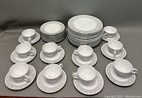 Overview of the full set showing stacked plates and arranged cups with saucers, displaying the matching silver or gray trim pattern on white china.