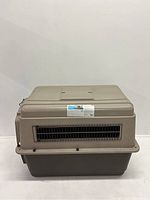 Large beige plastic and metal dog cage shown from front, with ventilation grid and label on top half.