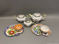 Photo of Nippon porcelain creamer, sugar bowl, teapot and two colorful luncheon sets with trays and cups.