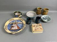 Overall view of nine ceramic items showing variety of styles and colors including decorative plate, bowls, mugs, cups, pitcher, and box.