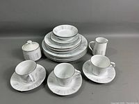 View of entire china set arranged showing all items included: stack of plates, bowls, cups on saucers, creamer, sugar bowl with lid.
