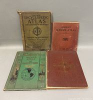 Front view of four atlas books showing front covers with titles and wear.