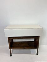 Full front view of the vintage drop leaf table showing the white Formica top and wooden base with caster wheels