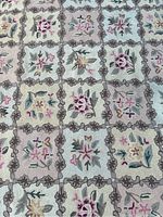 Close-up of floral grid pattern on the rug showing detailed hand hook stitching in muted pastel colors on beige background.