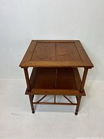 Side view of the vintage two-tier wooden side table showing the bottom shelf and round legs with support braces.