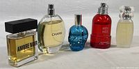 Wide shot showing all five perfume bottles, from left to right: Ambre Noir by Yves Rocher, Charm, blue skull bottle, More More in red bottle, small frosted bottle.