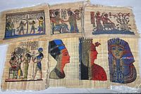 Seven Egyptian papyrus prints laid out showing colorful historic scenes and figures on natural papyrus, each about 17x12 inches, displayed in individual protective sleeves.