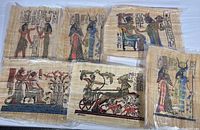 Photo showing all six papyrus prints in protective plastic sleeves with clear ancient Egyptian figures and hieroglyphs.