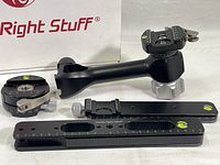 Photo showing the disassembled parts of the Really Right Stuff pano-gimbal head arranged in front of the branded storage box, highlighting the main arm, mounting plates, and adjustment knobs with scale markings and bubble levels.