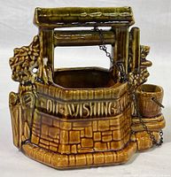 Front and side views of the brown glazed ceramic wishing well planter showing details of the stone texture, lettering, and attached bucket with chain.
