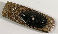 Money clip showing patterned inlaid metal and black carbon fiber with diamond accents in center
