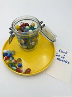 Jar filled with multicoloured marbles, extra marbles on yellow plate