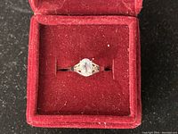 Top view of the 10kt gold ring with oval clear stone in red velvet ring box.