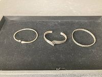 Photo of three silver bracelets on a black surface.