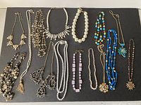 Full view of the collection of costume jewelry laid out on a dark surface, showing the variety of necklace styles, bracelets, colors, and materials.