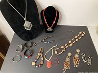 Full view of mixed costume jewelry collection on display, including necklaces, bracelets and earrings arranged on a black surface and bust forms.
