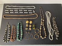 Collection of assorted costume jewelry including necklaces and earrings laid out on dark surface.